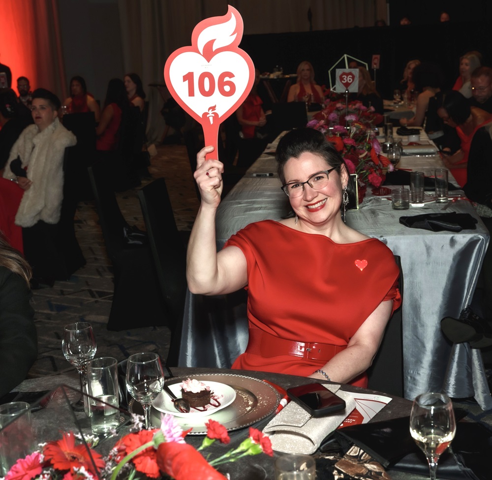 Sarah Jo Brockhouse seated at a table holding up bidder paddle number 106.